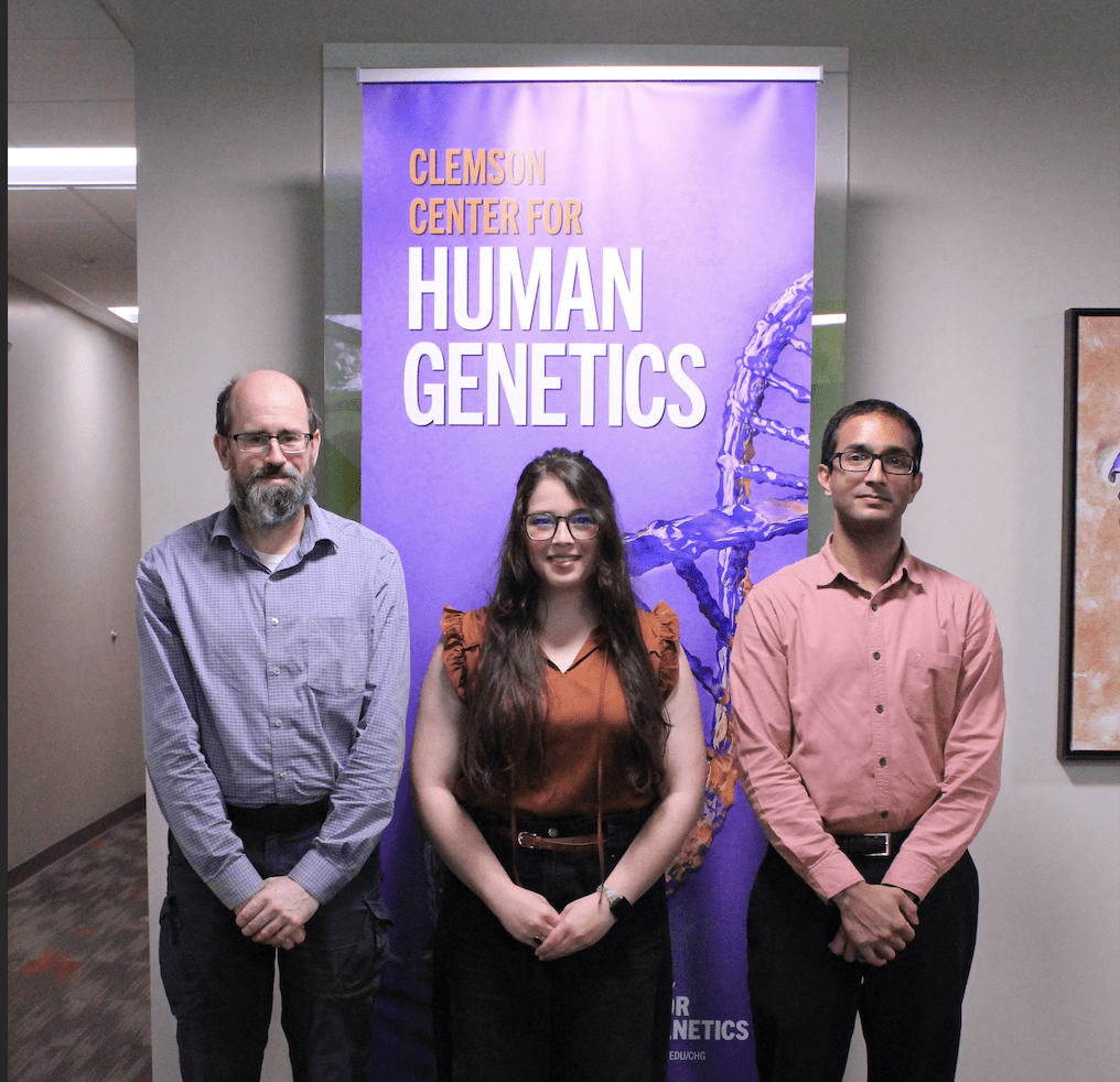 One woman and two men stand in front of a purple banner that says Center for Human Genetics.