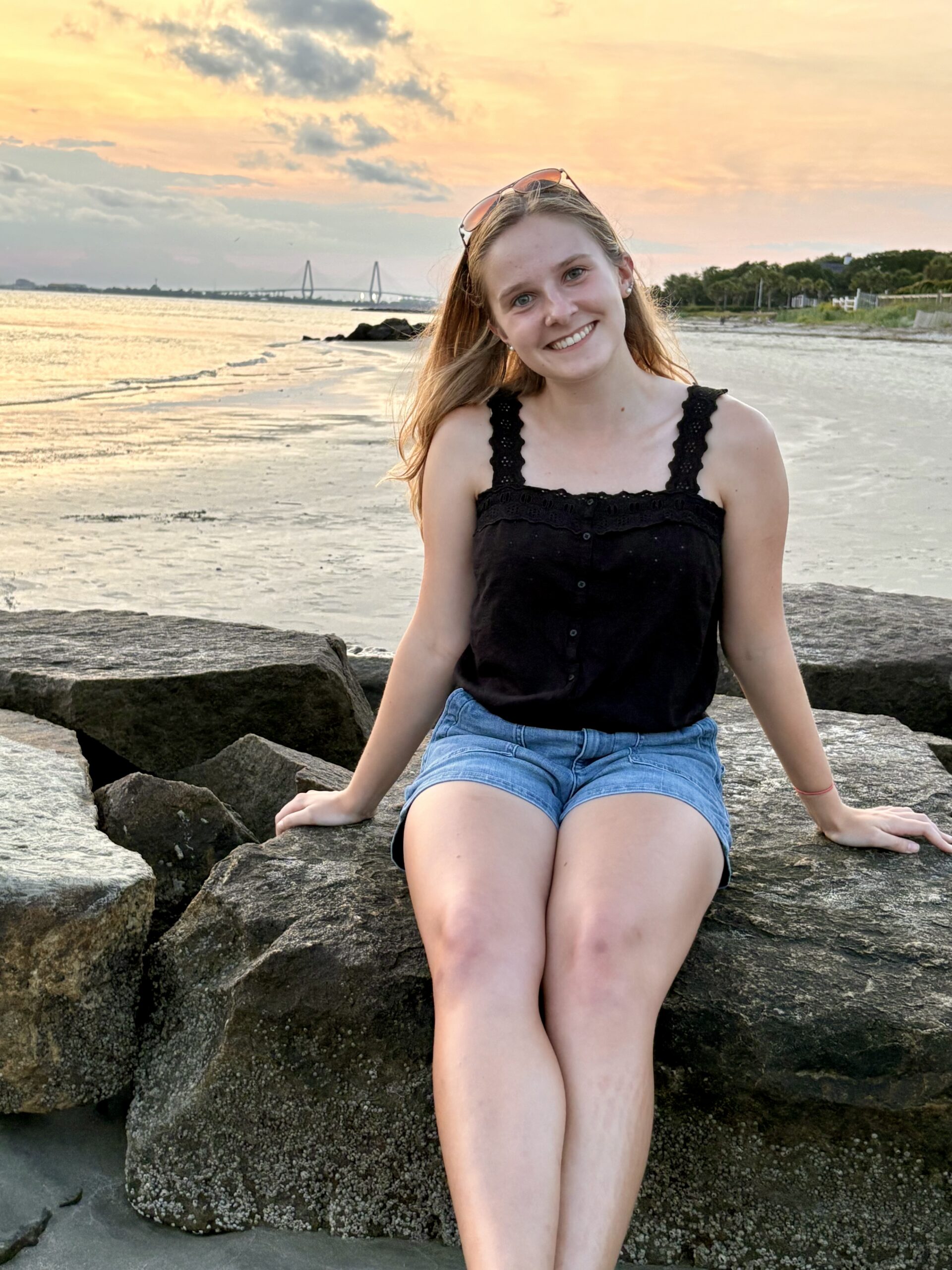 Kaylee Wilson sitting on a boulder with the beach and ocen behind her at sunset