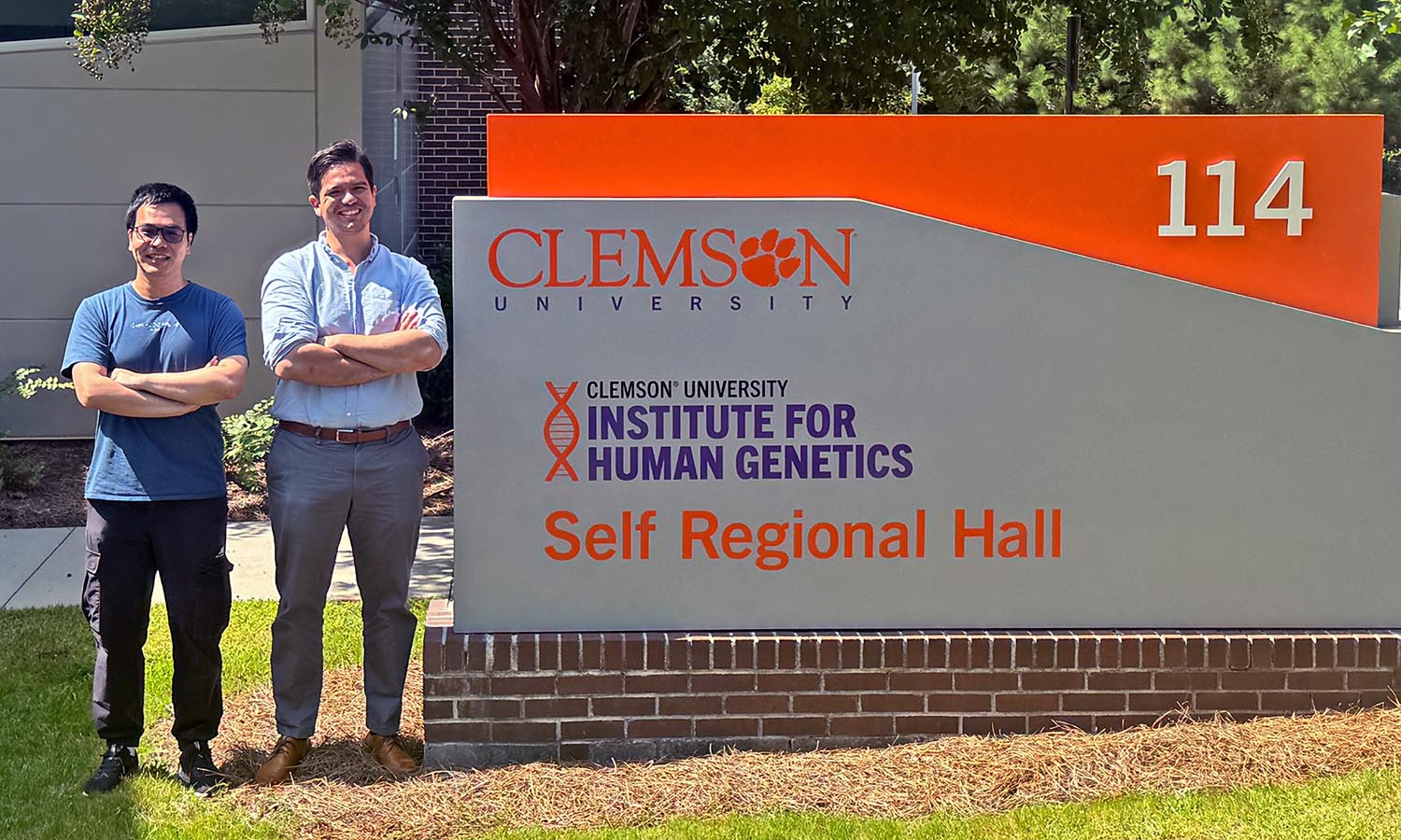 ihg research jiping carlos Two men stand beside a sign for Clemson University’s Institute for Human Genetics at Self Regional Hall, building 114.