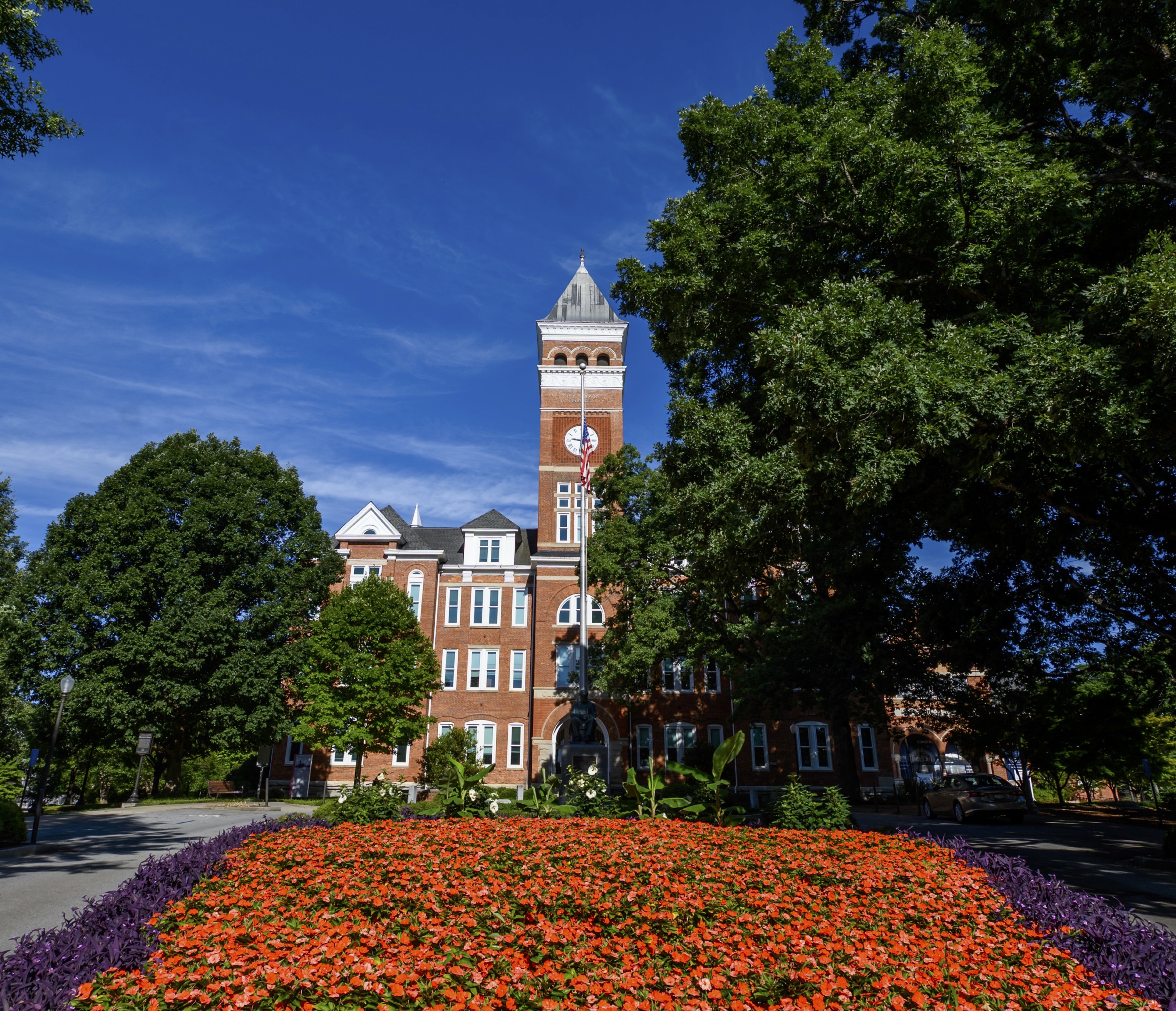Picture of a red brick building with a field of flowers in front and a large tree.