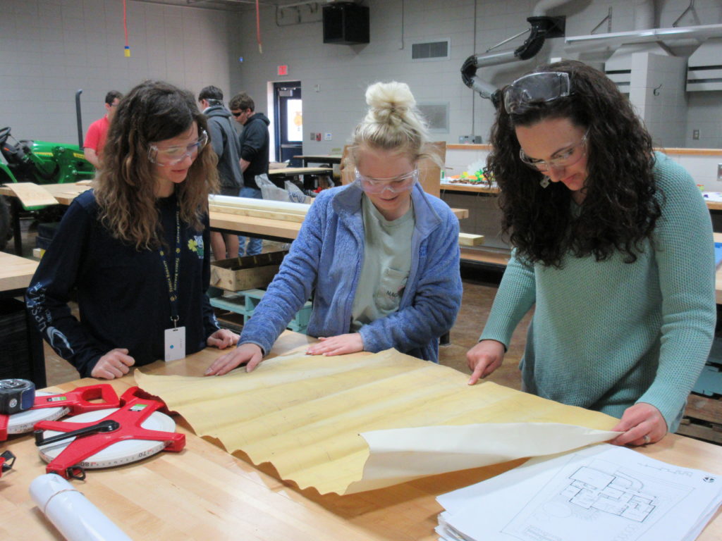 Students learning about carpentry plans from teacher